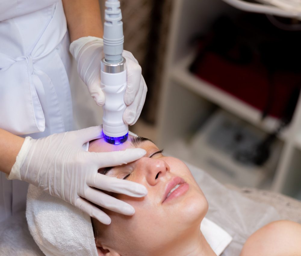 A young beautiful girl lies on the beautician's table and receives procedures with a professional apparatus for skin rejuvenation and moisturizing